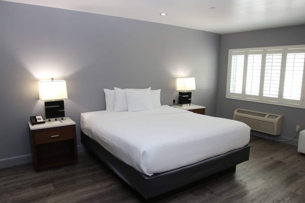 Een moderne slaapkamer met een groot bed, twee nachtkastjes met lampen, een raam met zonwering en een wandairconditioner.
