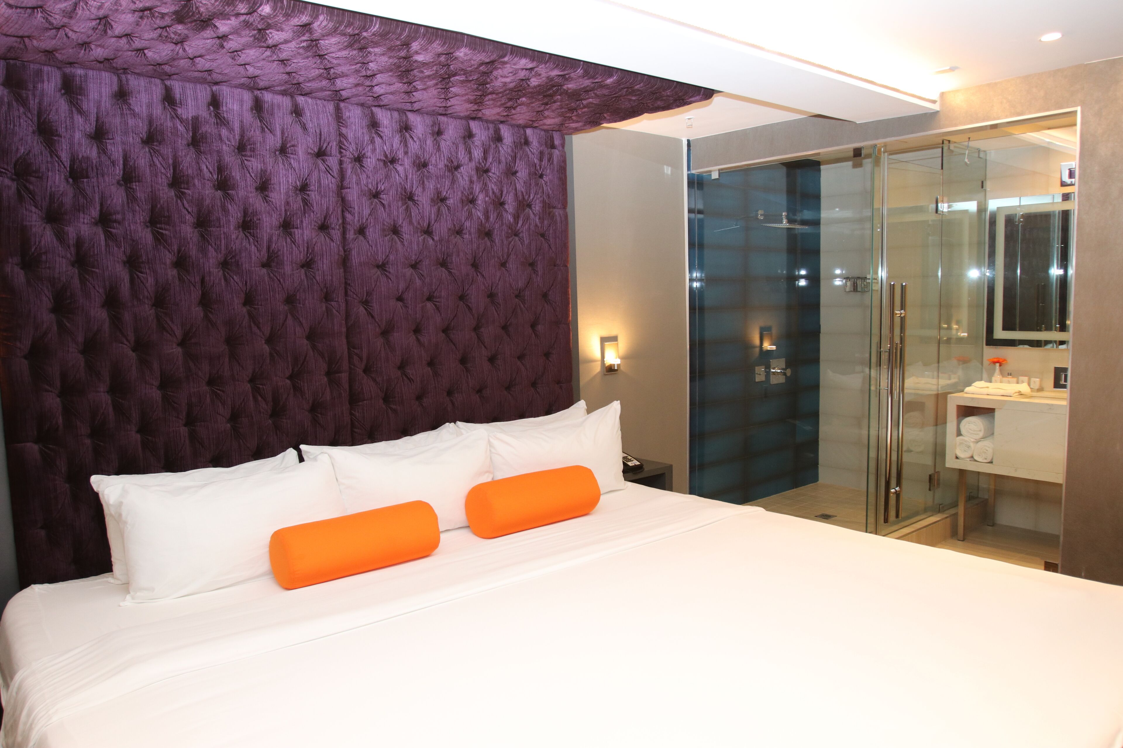A hotel room with a large bed, a glass shower enclosure, and a modern bathroom.