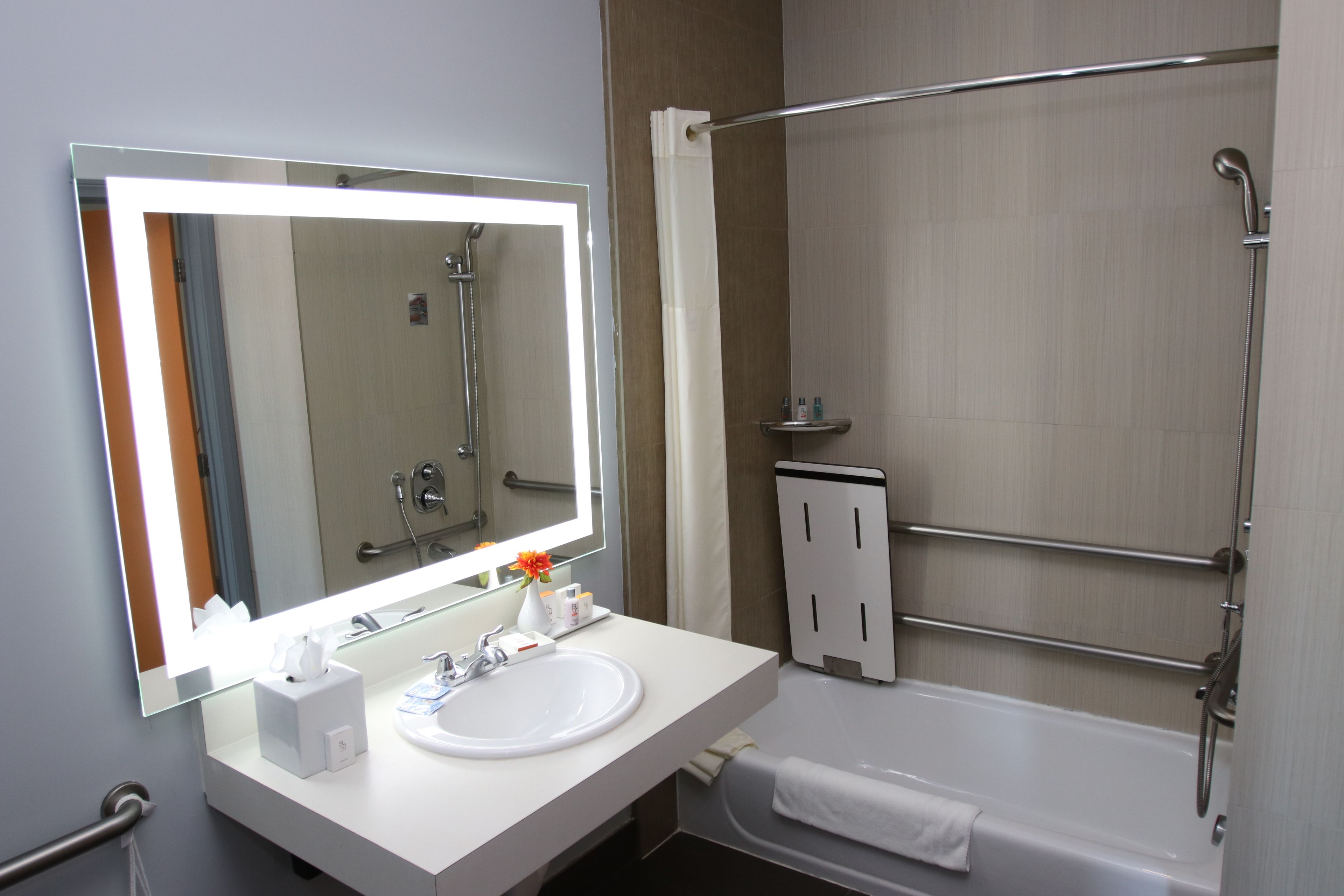 Een moderne badkamer met een witte wastafel, een grote spiegel, een douche met glazen deur en een handdoekrek.