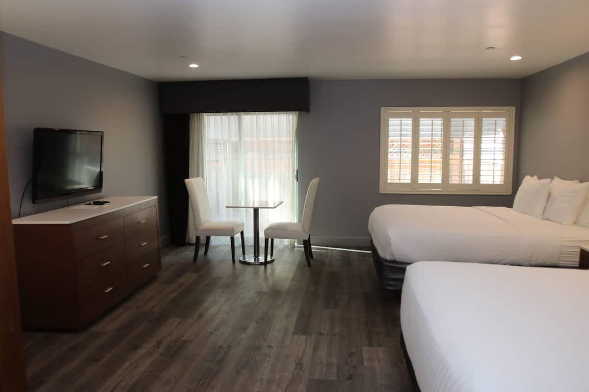 Een hotelkamer met een televisie, bureau, twee stoelen, bed en raam.