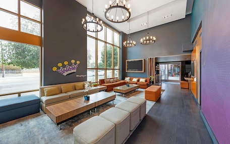 A spacious lobby with a large seating area, modern chandeliers, and large windows offering a view of the outdoors.