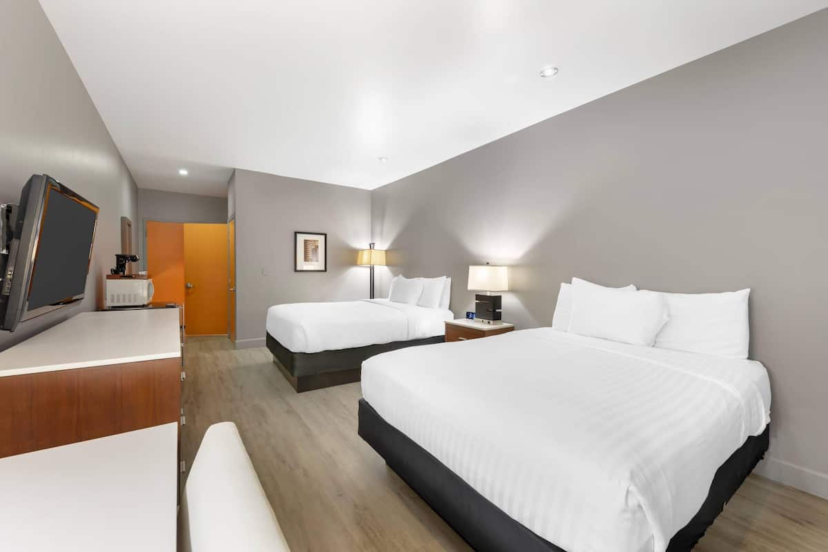 Een hotelkamer met een groot bed, een kleiner bed, een bureau met een computer en een televisie.