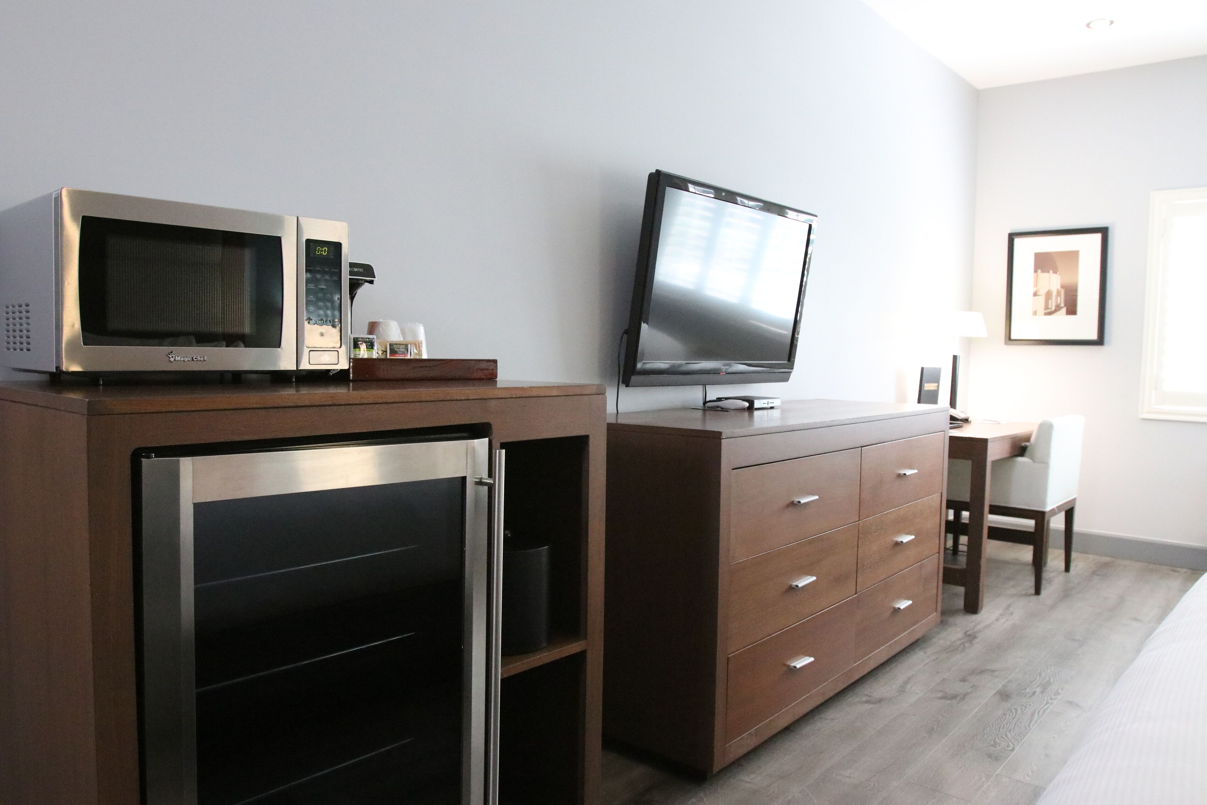 A modern kitchen with a microwave, a refrigerator, and a flat-screen TV on a wooden cabinet.