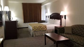 Habitación de hotel con cama, escritorio, silla, lámpara y un ventanal con cortinas.