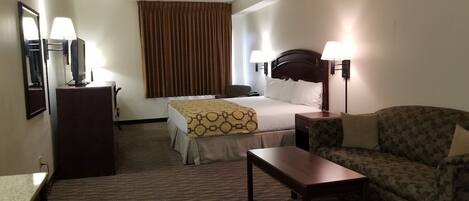 A hotel room with a bed, a desk, a chair, a lamp, and a large window with curtains.