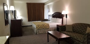 A hotel room with a bed, a desk, a chair, a lamp, and a large window with curtains.