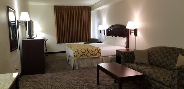 Habitación de hotel con cama, escritorio, silla, lámpara y un ventanal con cortinas.