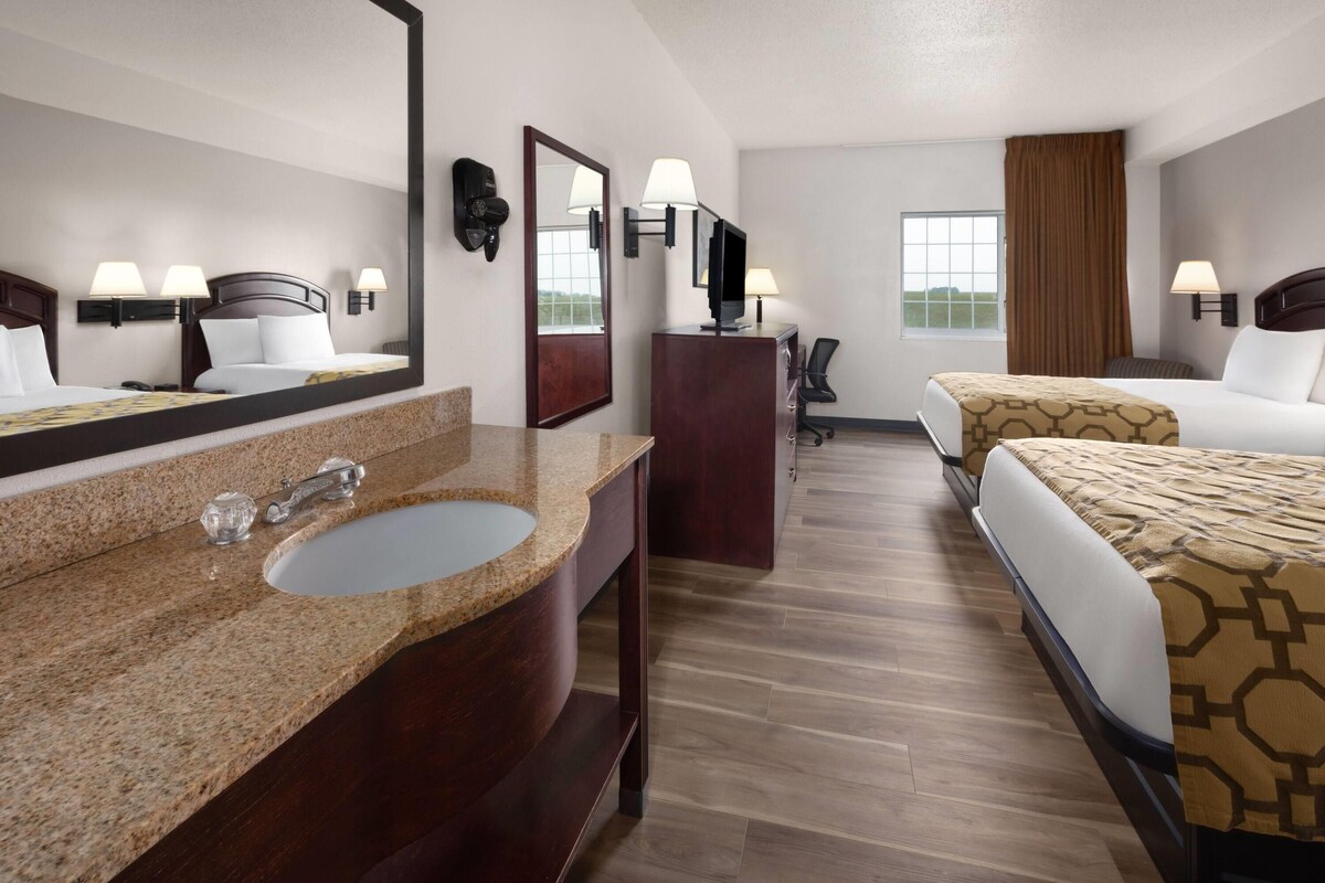 A hotel room with a large mirror, two beds, a desk, and a window.