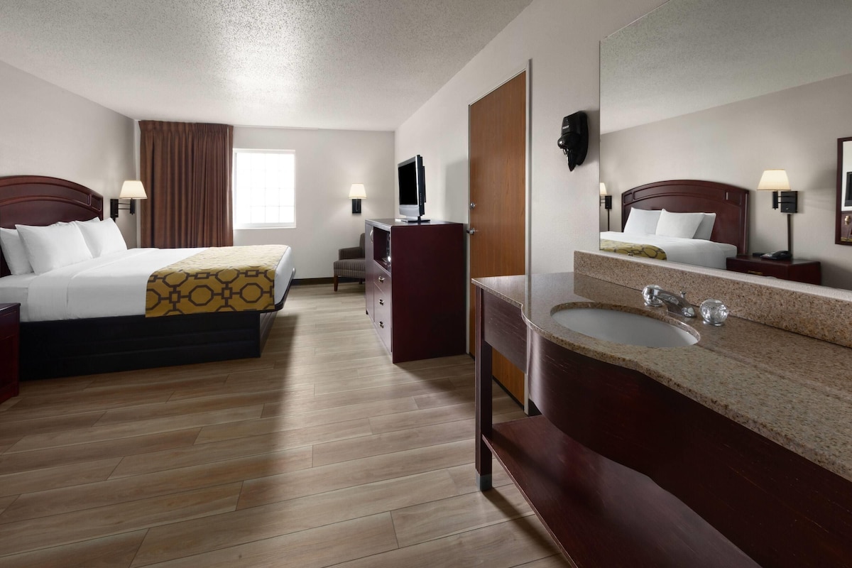A hotel room with two beds, a desk, a TV, a bathroom with a sink and mirror, and a window.