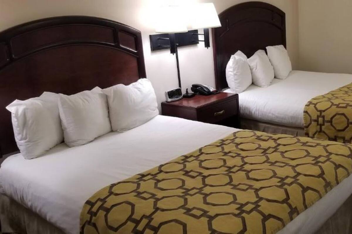 A hotel room with two beds, each with white bedding and a patterned duvet cover. There is a nightstand with a lamp and a telephone.