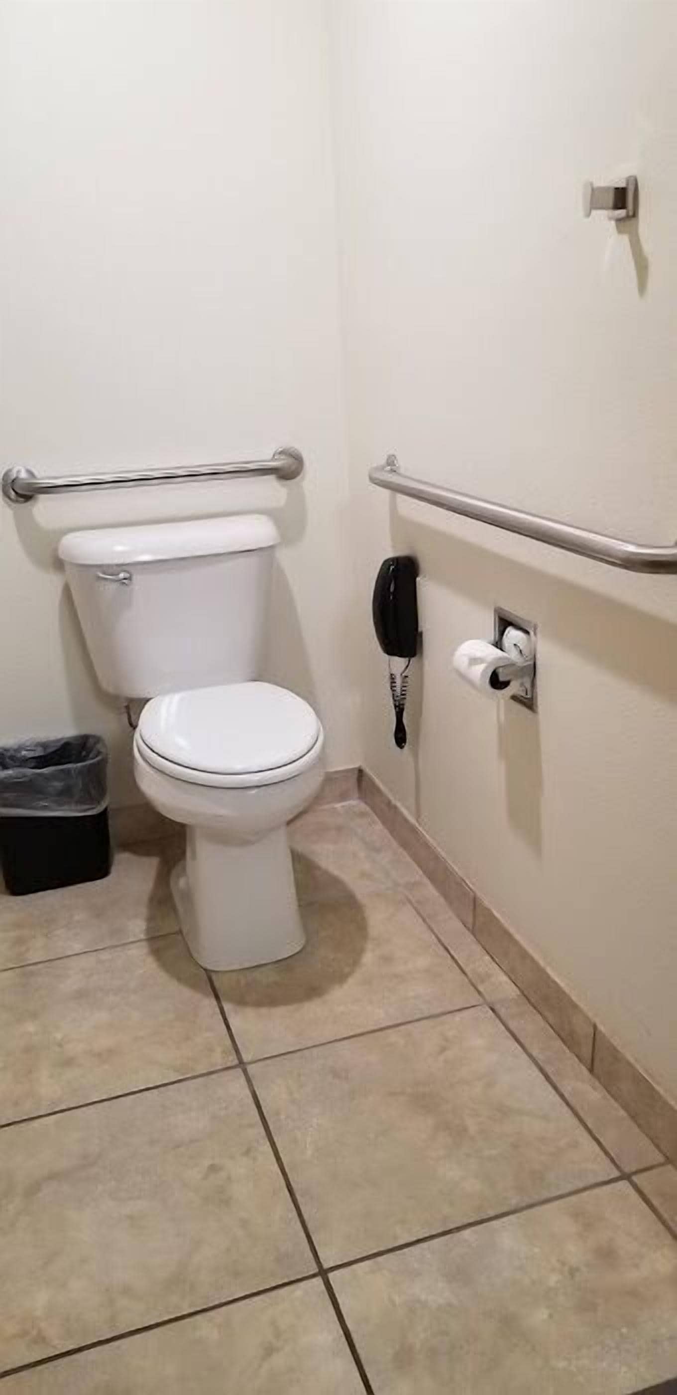 A small, clean bathroom with a white toilet, a trash bin, a hand dryer, and a paper towel dispenser.