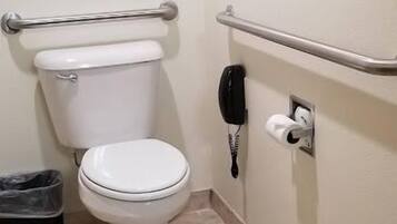 A small, clean bathroom with a white toilet, a trash bin, a hand dryer, and a paper towel dispenser.