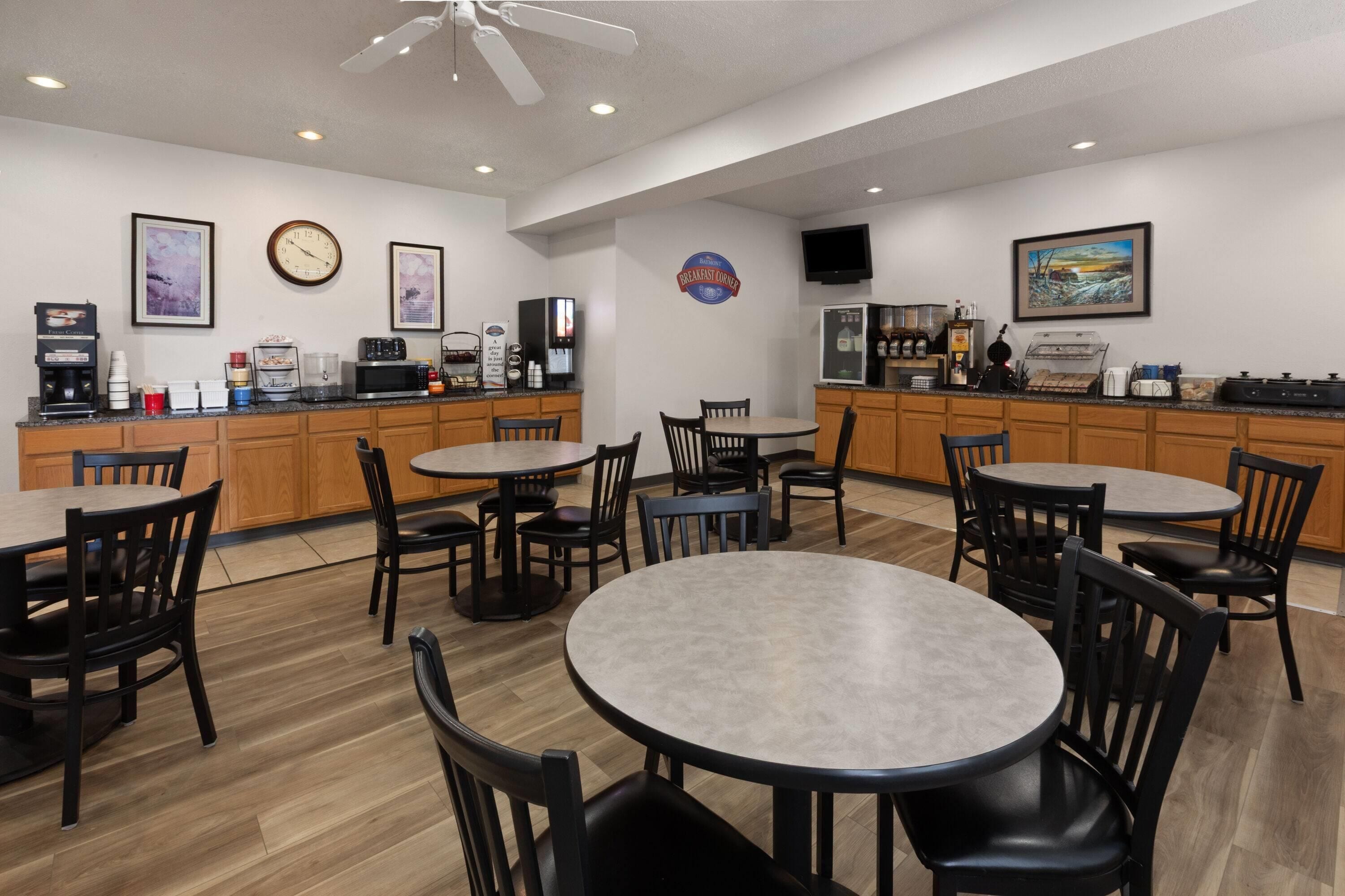 A breakfast area with tables, chairs, a coffee machine, a microwave, and a refrigerator.