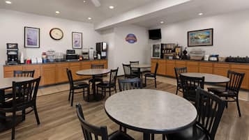 A breakfast area with tables, chairs, a coffee machine, a microwave, and a refrigerator.