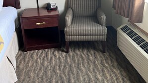 Een hotelkamer met een bed, een nachtkastje met een lamp, een gestreept fauteuil en een radiator.