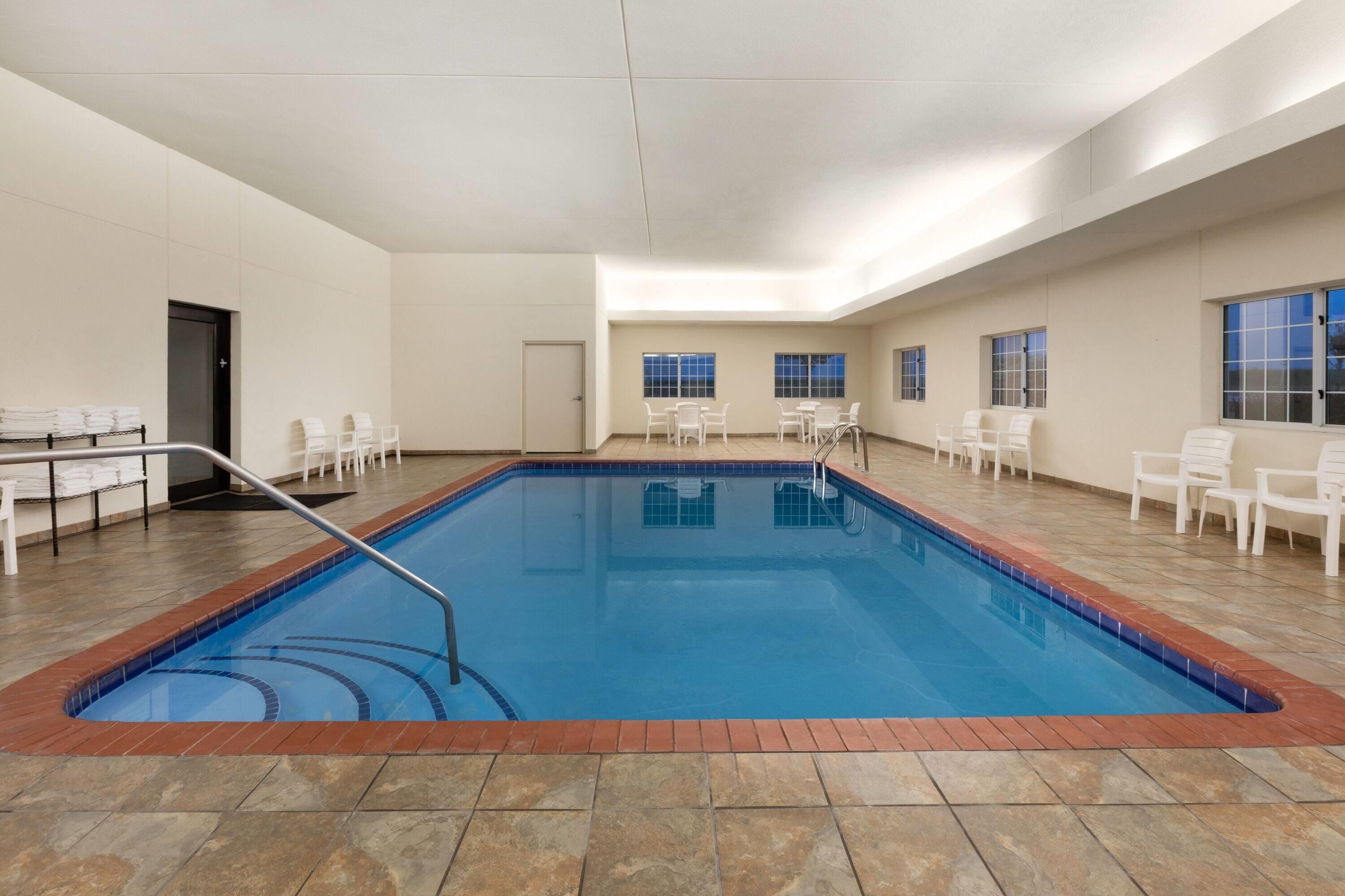Una piscina interior con suelo de baldosas, rodeada de sillas blancas y una puerta.