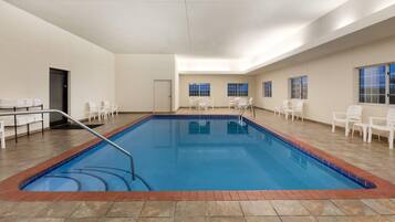 Una piscina interior con suelo de baldosas, rodeada de sillas blancas y una puerta.