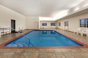An indoor swimming pool with a tiled floor, surrounded by white chairs and a door.