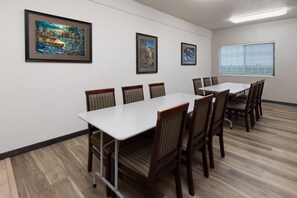A conference room with a white table and chairs, framed artwork on the walls, and a window with blinds.