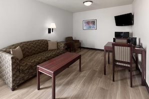 A furnished living room with a sofa, a coffee table, a TV, and a small table with a chair.