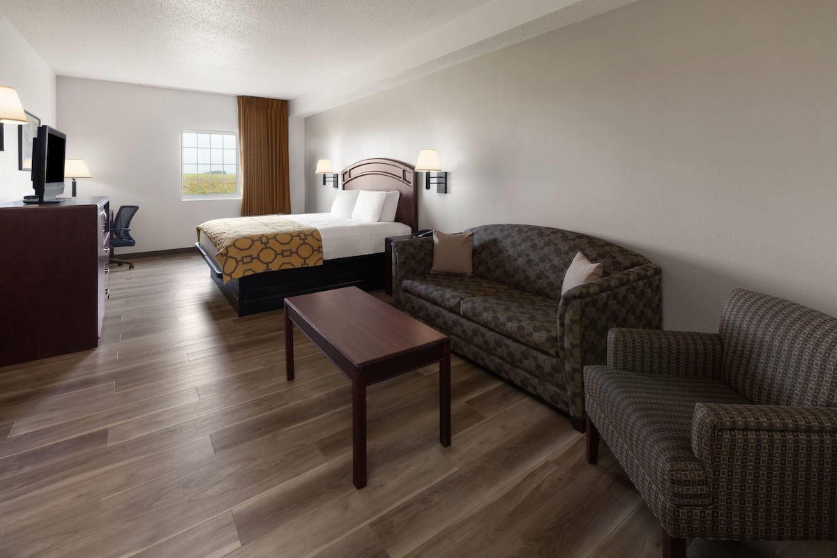A hotel room with a bed, a sofa, a coffee table, and a desk with a lamp.