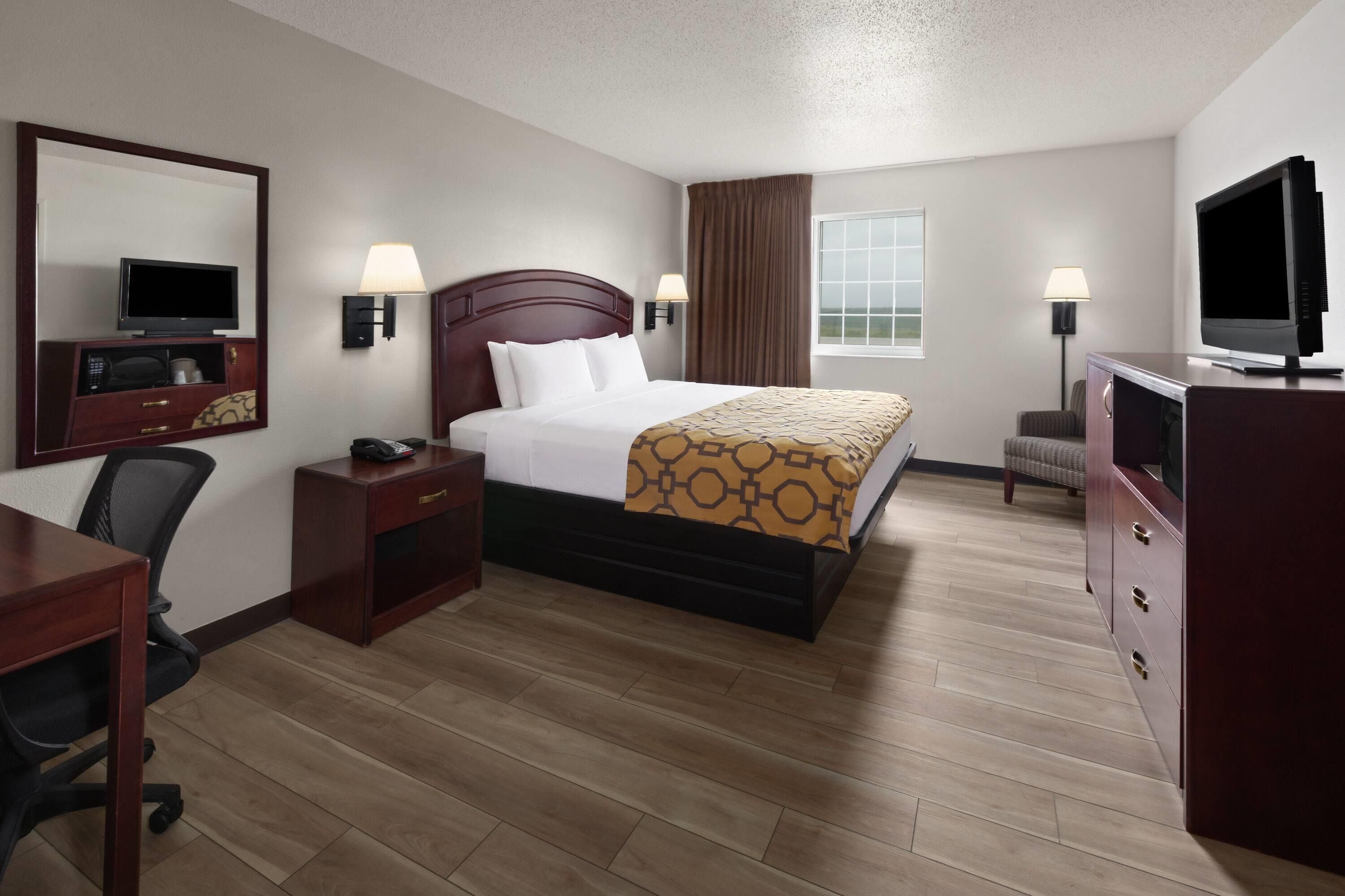 A hotel room with a bed, bedside tables, a desk, a television, and a window with curtains.