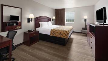 A hotel room with a bed, bedside tables, a desk, a television, and a window with curtains.