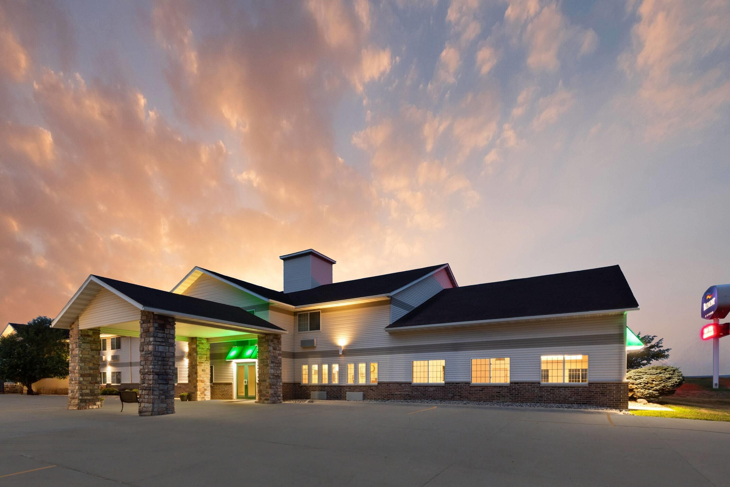 A hotel with a central entrance, multiple windows, and a parking lot.