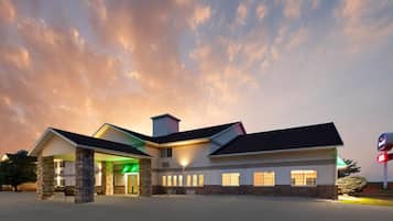 A hotel with a central entrance, multiple windows, and a parking lot.