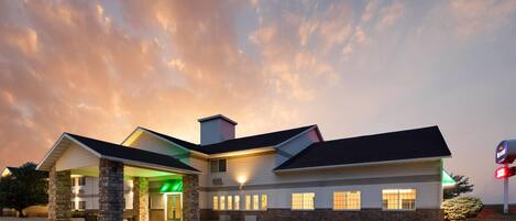 A hotel with a central entrance, multiple windows, and a parking lot.