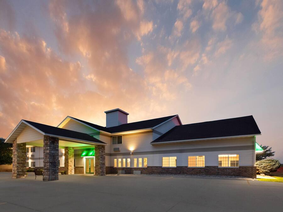 A hotel with a central entrance, multiple windows, and a parking lot.