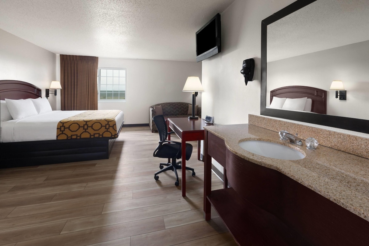 A hotel room with a bed, a desk, a chair, a bathroom with a sink and mirror, and a television mounted on the wall.