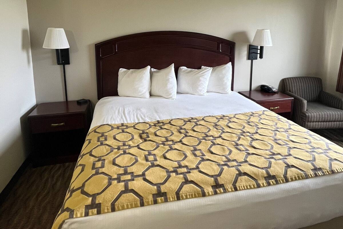 A hotel room with a large bed, two bedside tables, a chair, and two lamps.