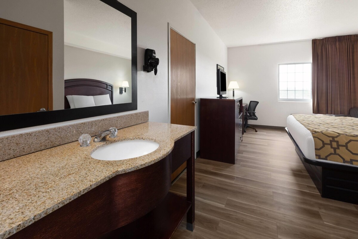 A hotel room with a bed, a desk, a television, a bathroom with a sink and mirror, and a large window.