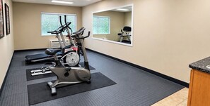 Een sportschool met cardiotoestellen, een spiegel en een raam met jaloezieën.