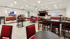 A spacious dining area with multiple tables and chairs, a kitchen area with a TV, and a breakfast bar with food items.