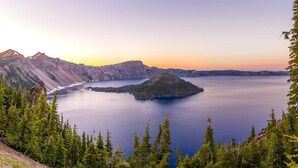 Un paisaje montañoso con un gran lago, rodeado de bosques densos y terreno rocoso.