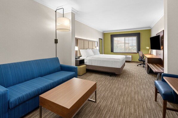A hotel room with a bed, a blue sofa, a wooden table, a desk with a chair, a TV, and a window with a view. - Holiday Inn Express & Suites Klamath Falls Central by IHG (Klamath Falls)