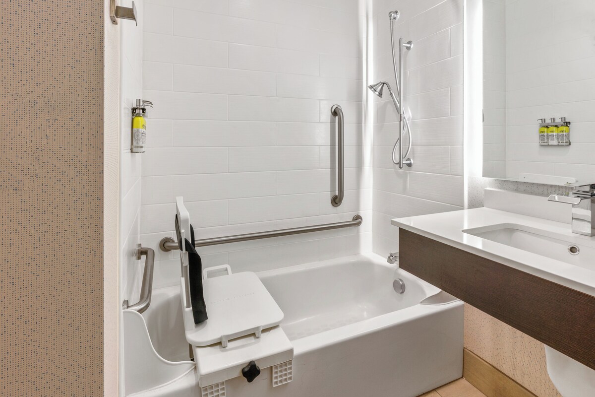 A modern bathroom with a walk-in shower, grab bars, a white bathtub, and a vanity with a mirror.