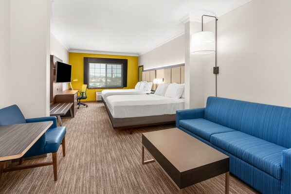 A hotel room with a bed, a blue sofa, a desk with a chair, a TV, and a window.