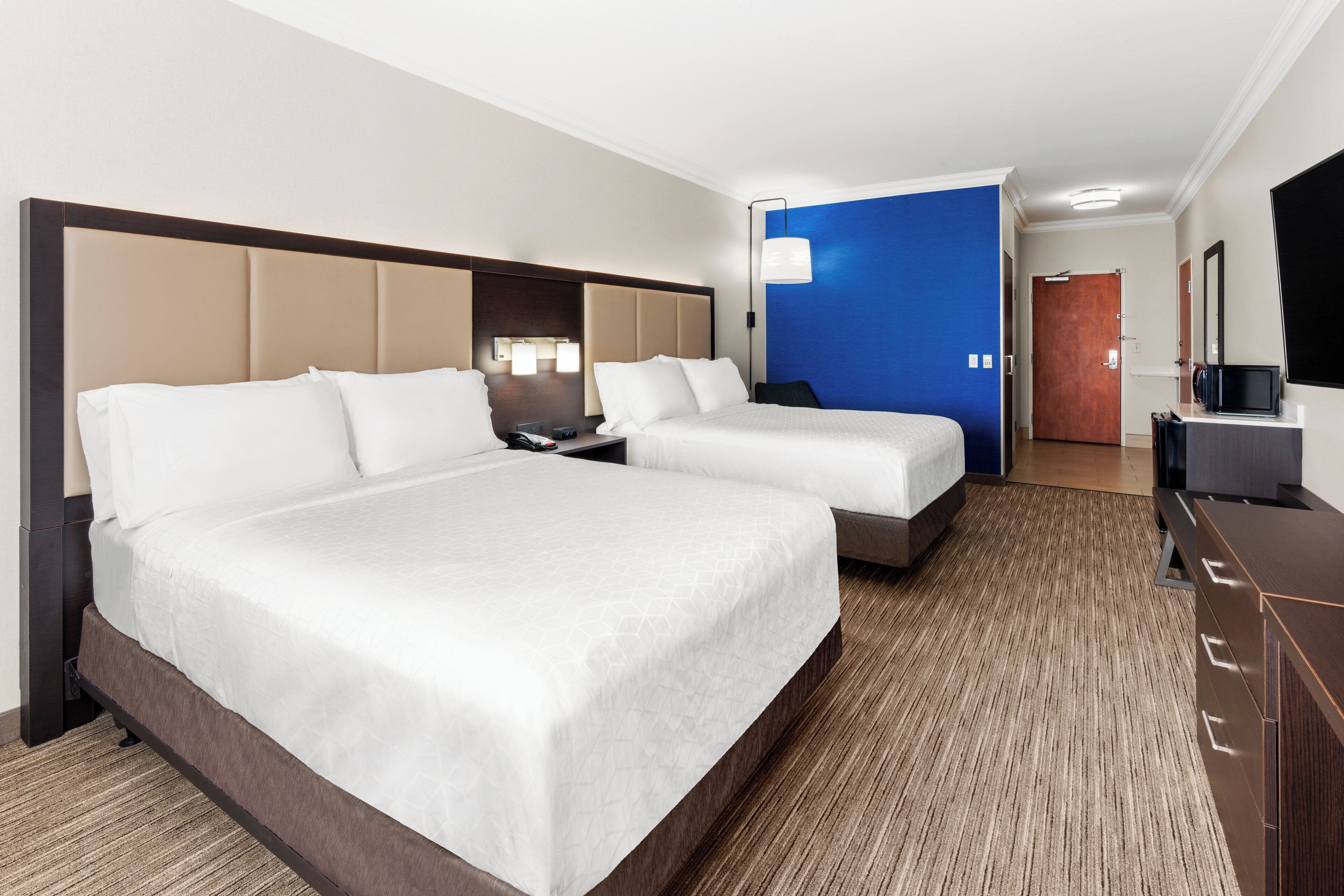 Une chambre d’hôtel avec un grand lit, un lit plus petit, un bureau, une télévision et une porte de salle de bain.