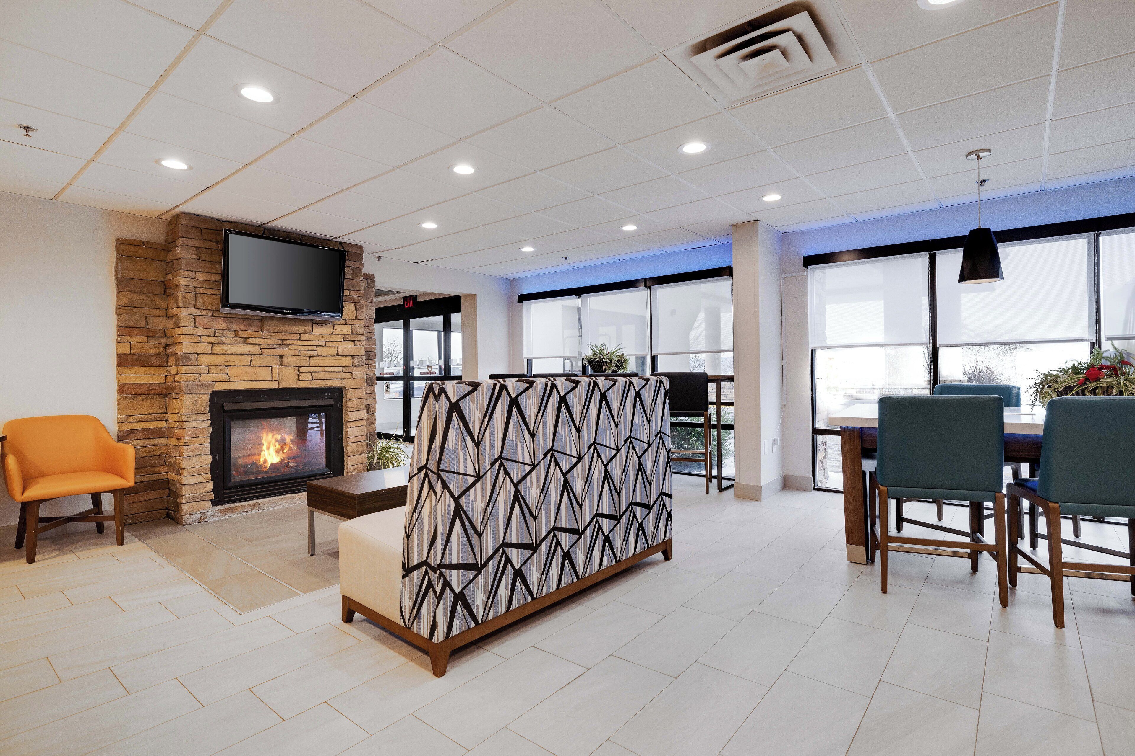 Un vestíbulo moderno con chimenea de piedra, televisor de pantalla plana, separador decorativo y zona de comedor con sillas y mesa.
