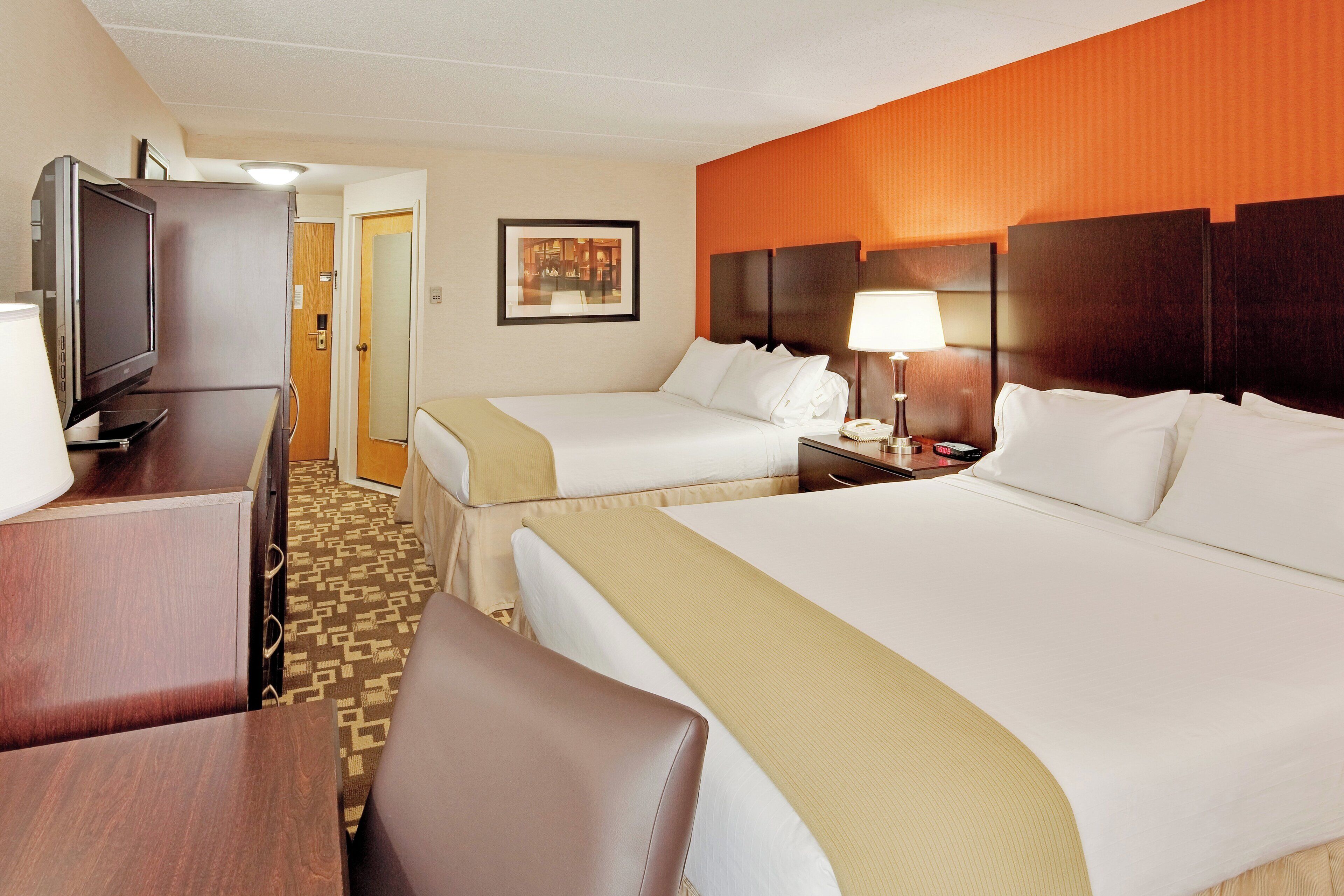 Een hotelkamer met twee bedden, een bureau met een televisie, een lamp en een wekker.