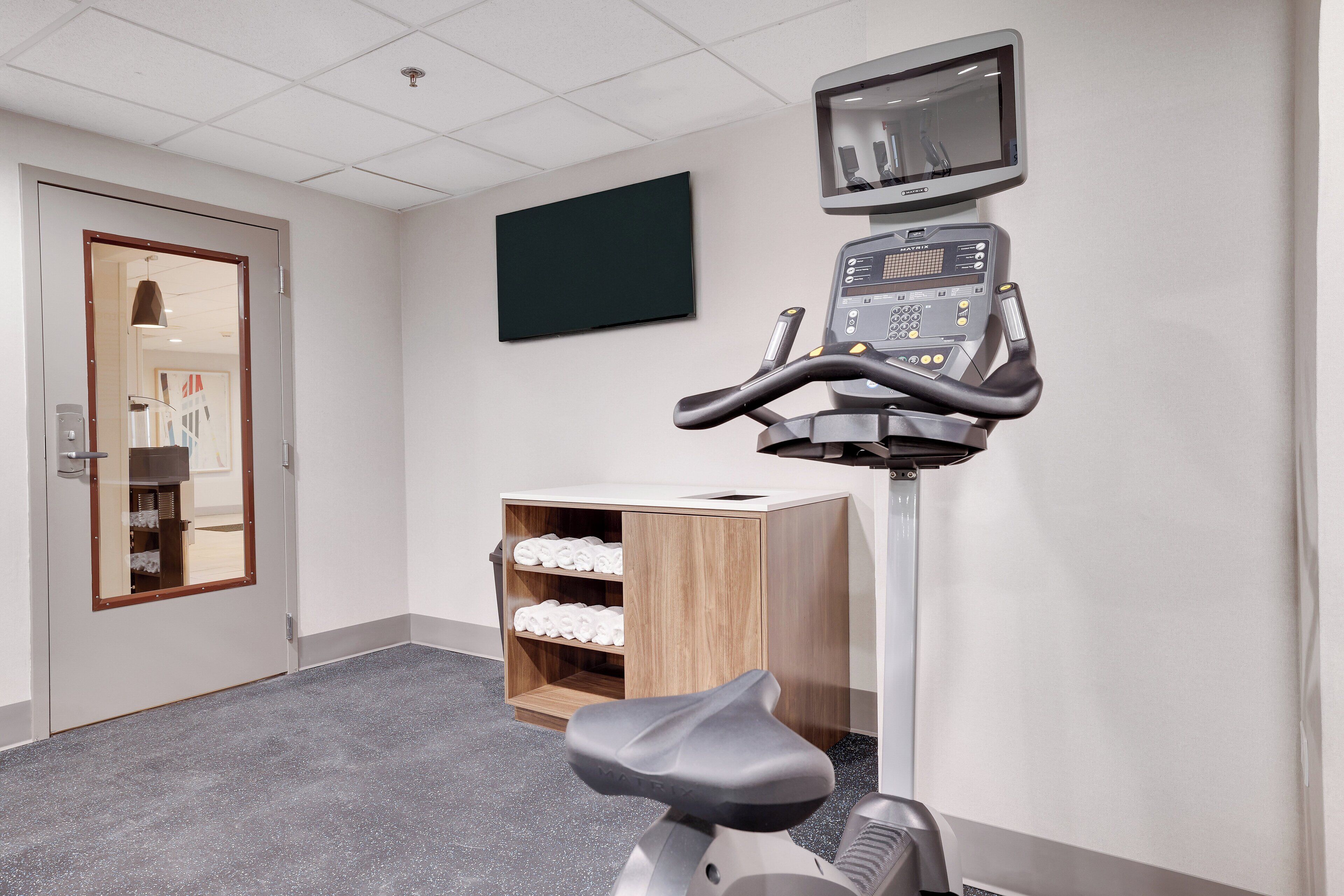 A fitness room with a stationary bike, a treadmill, and a mirrored wall.