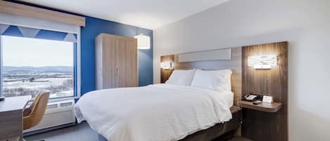 Una habitación de hotel moderna con una cama grande, un escritorio con silla, un armario y vistas a la ciudad a través de un ventanal amplio.