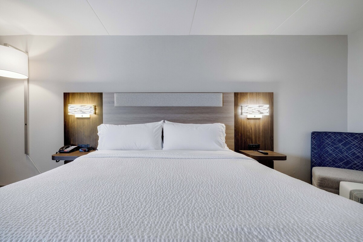 Quarto de hotel com uma cama grande, duas mesas de cabeceira com luminárias e cabeceira com iluminação embutida.