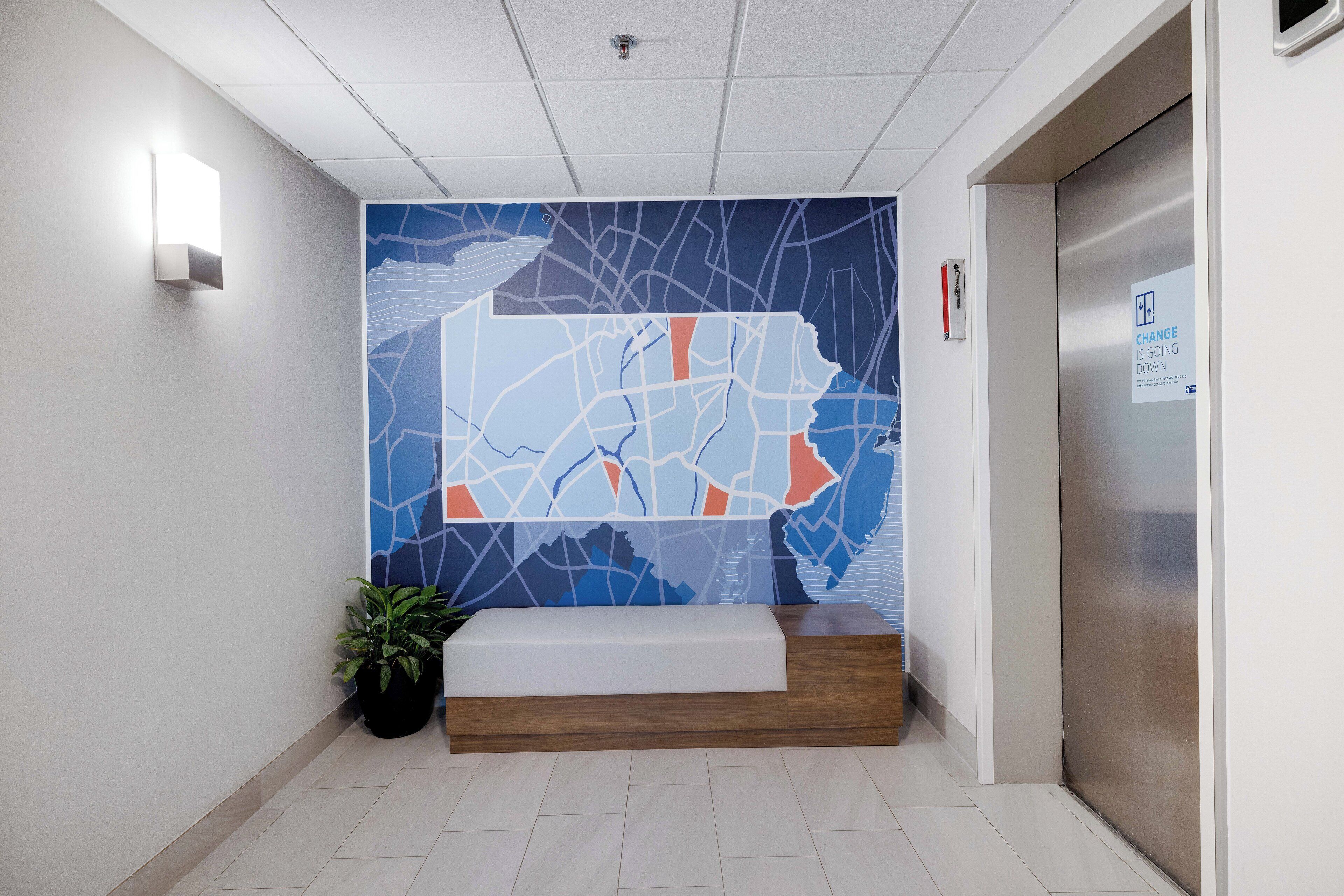 Zona de recepción con un mural de mapa, mostrador de recepción, planta en maceta y un ascensor.
