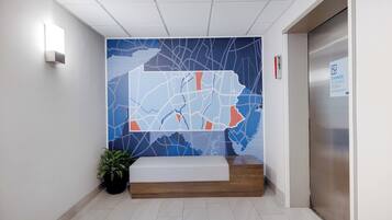 Zona de recepción con un mural de mapa, mostrador de recepción, planta en maceta y un ascensor.