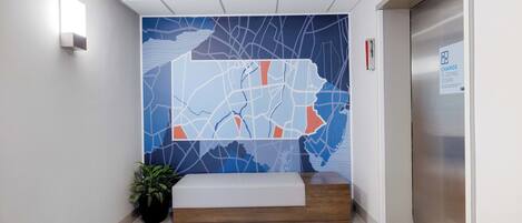 Zona de recepción con un mural de mapa, mostrador de recepción, planta en maceta y un ascensor.