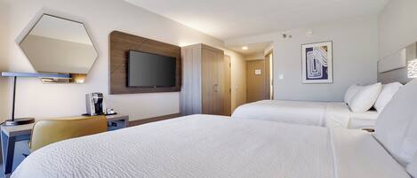 A hotel room with two beds, a desk with a lamp, a flat-screen TV, and a wooden panel wall.